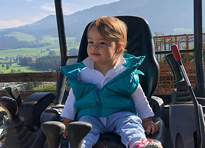 Kleinkind sitzt auf Minibagger vor Alpenkulisse